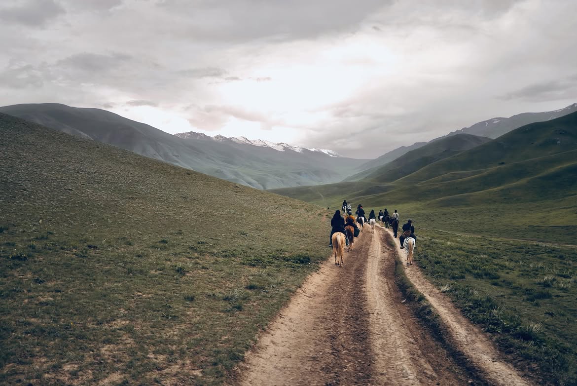 Riders on a mountain track heading toward snow-capped peaks