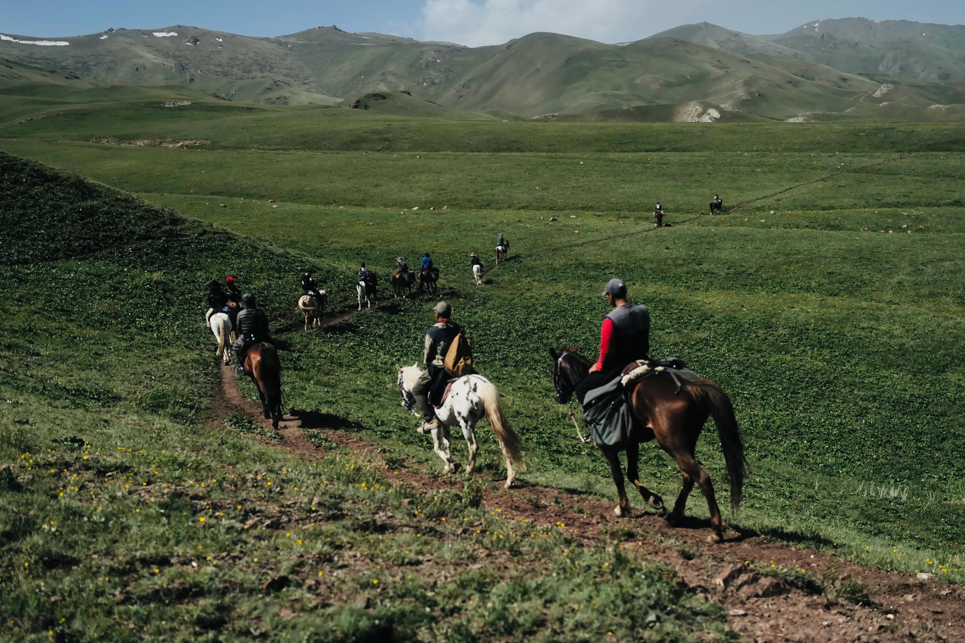 A group of riders descending into a green valley in the Tien Shan mountains