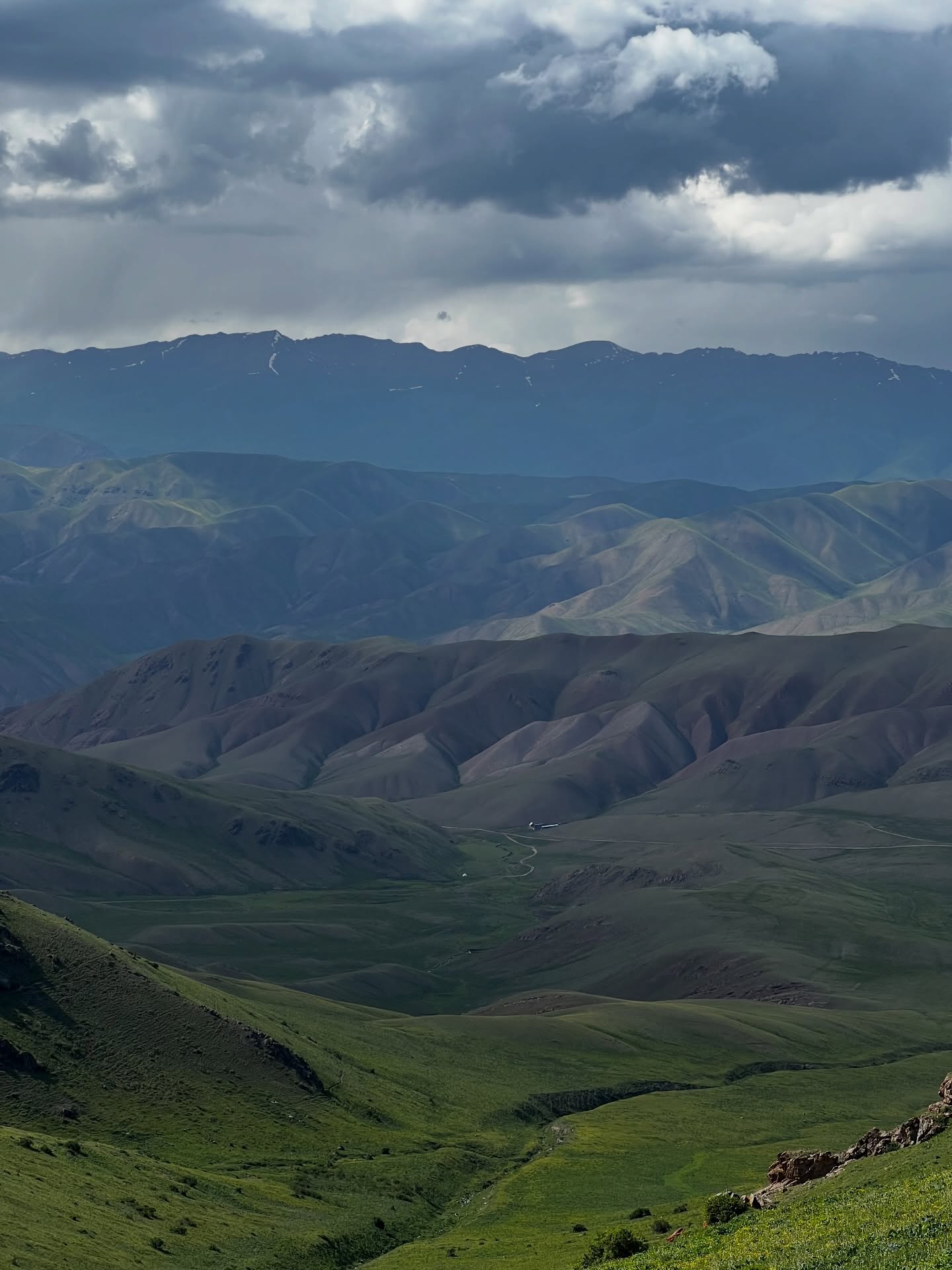 Green valleys and brown ridges below a mountain range in storm light