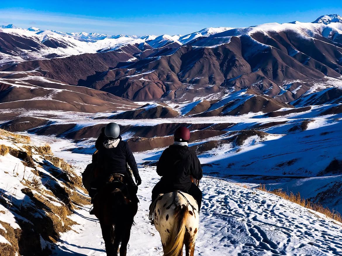 Two riders on a snowy ridge above the winter Tien Shan